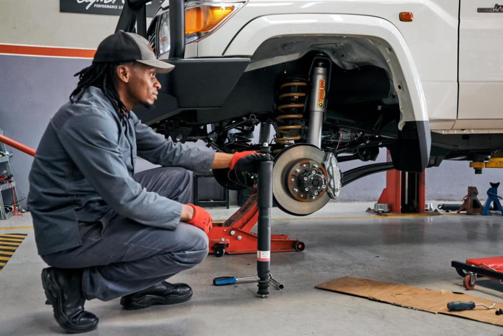 Hi-Range technician inspecting the front suspension of a 4x4 on a workshop hoist